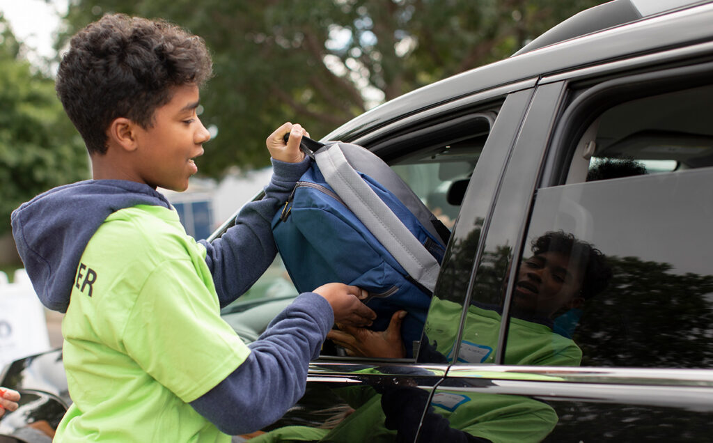 Young Volunteers handing out free backpacks through a car window.