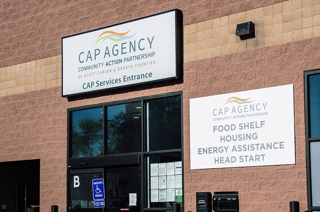 Exterior view of the CAP Agency brick building featuring signs for the CAP Services Entrance, Food Shelf, Housing, Energy Assistance, and Head Start.