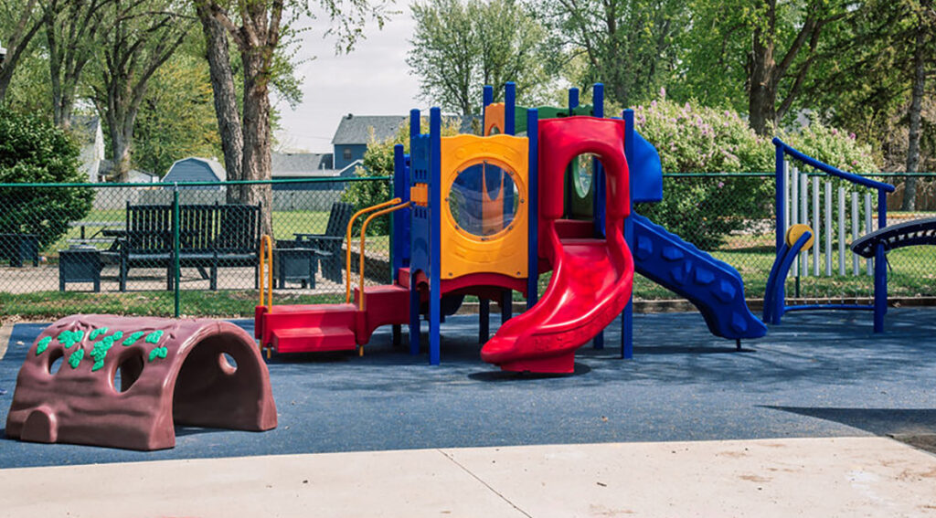 A colorful playground structure with a red slide and a blue slide on a sunny day