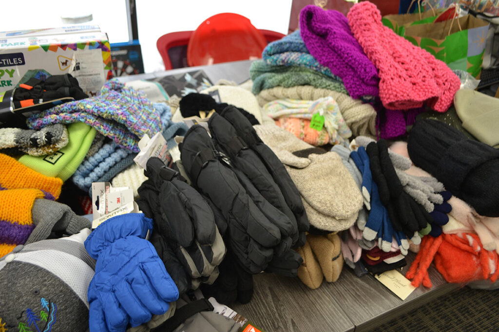 A pile of winter clothing items including colorful gloves, mittens, and knit hats on a table.