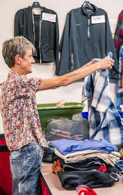 An older female volunteer sorting clothes on a rack at the Local Imports Thrift Store.