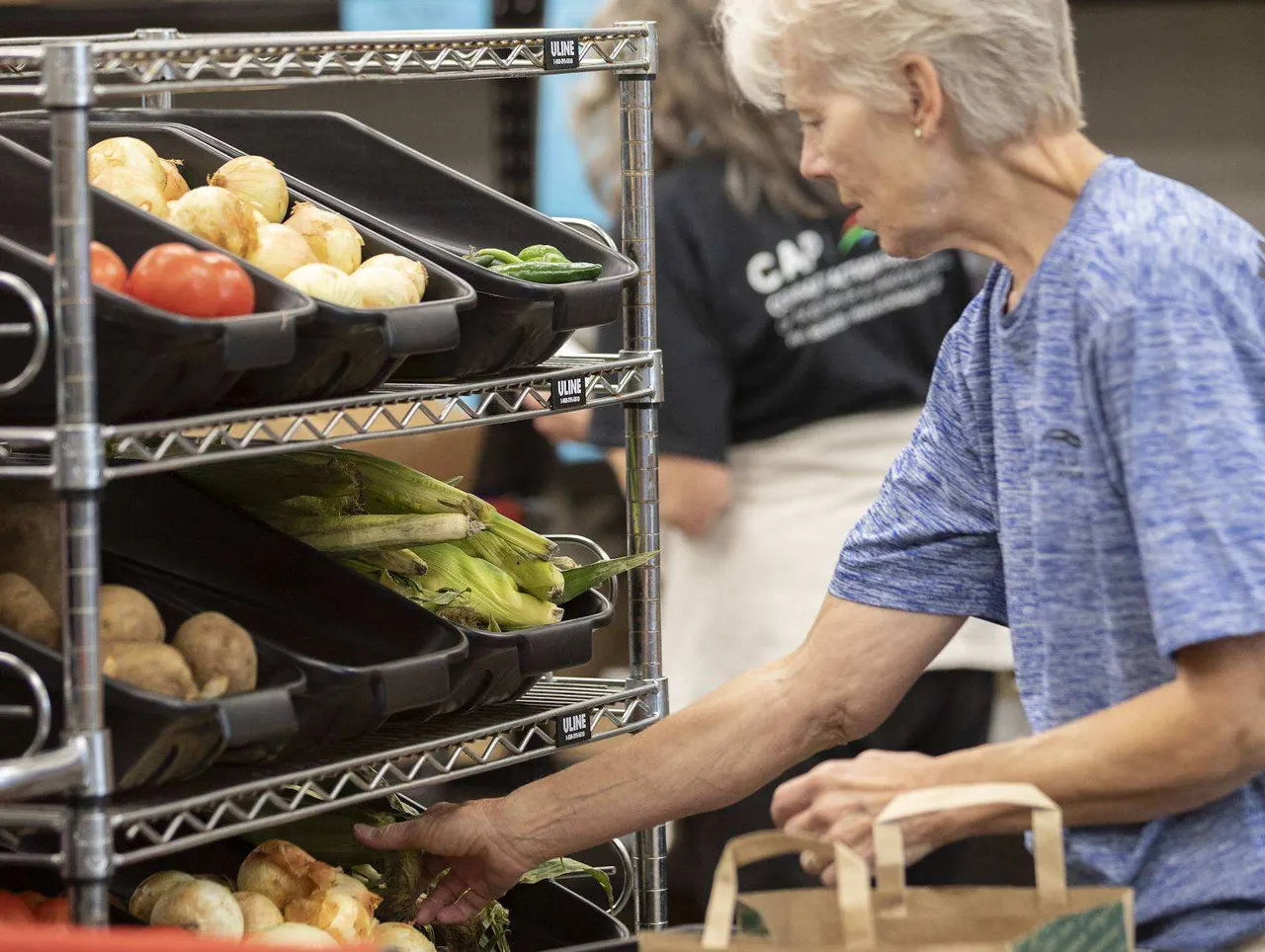 A CAP Agency volunteer organizing fresh produce in bins on a metal shelf.