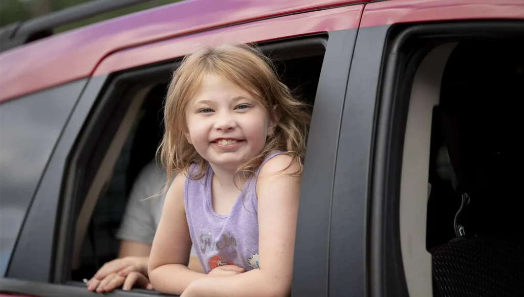 A young girl smiling out the window of a vehicle.