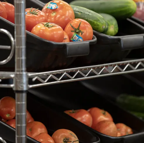 resh produce, including red tomatoes and green vegetables, displayed in black bins on a metal rack.