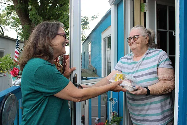 Volunteer delivering a care package to an elderly resident at their doorway during the holiday program.